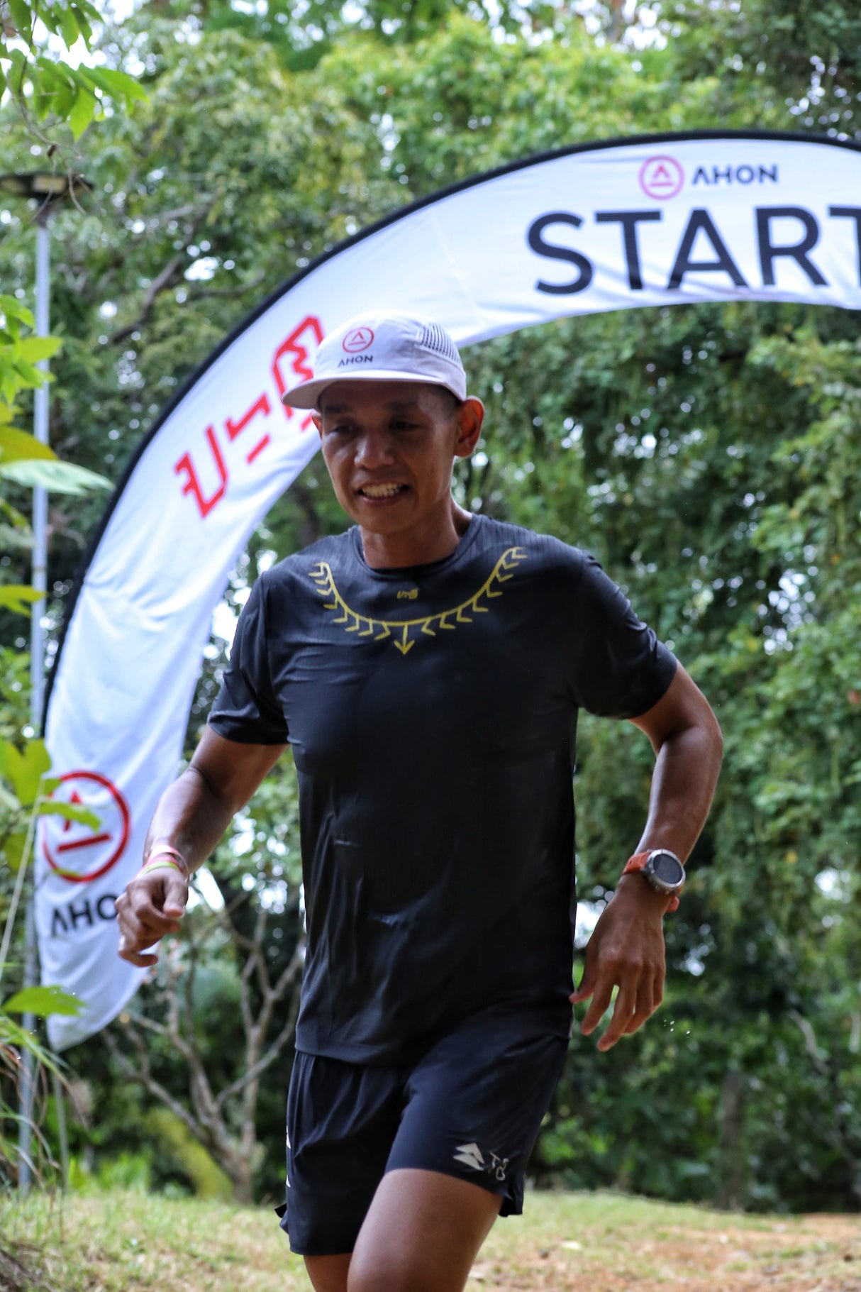 Male trail runner wearing Ahon’s Koling Super Light SS Shirt in black/gray with yellow collar detail during a mountain race.