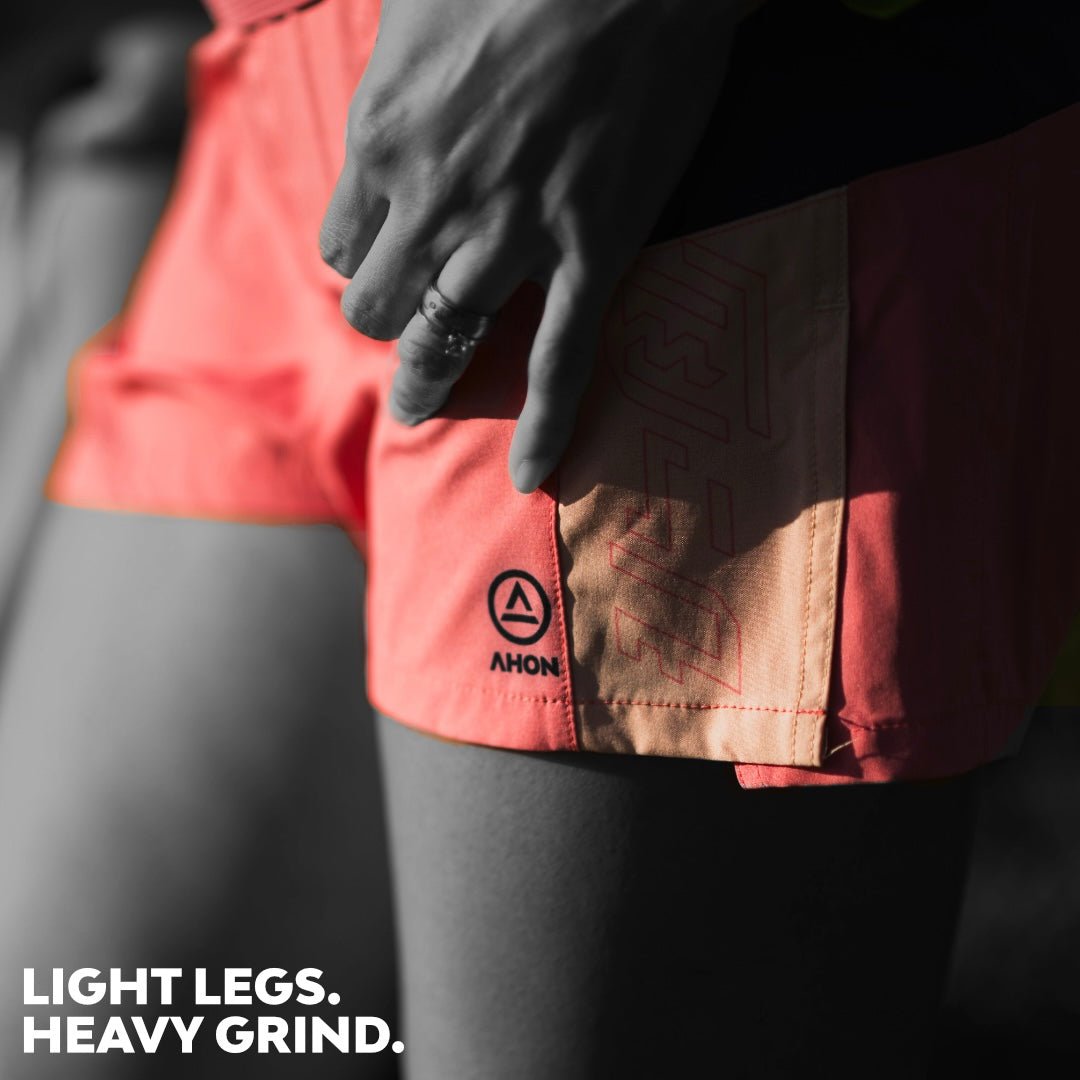 Close-up of hand resting on Ahon Trail Shorts Pro with coral and peach panel design