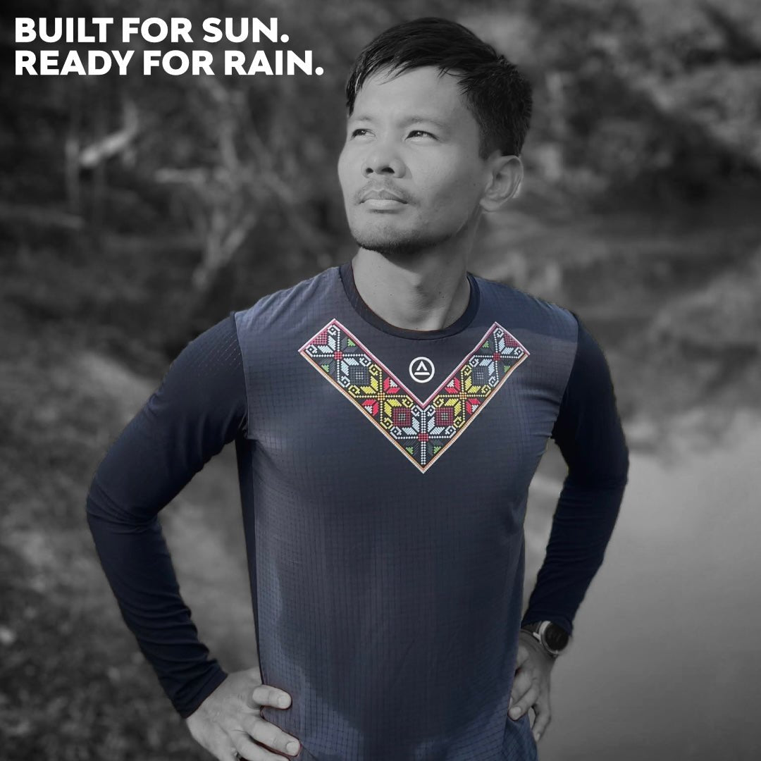 Male trail runner wearing Uleyan Super Light LS Shirt in dark gray, standing on a forest trail with overlay text “Built for Sun. Ready for Rain.”