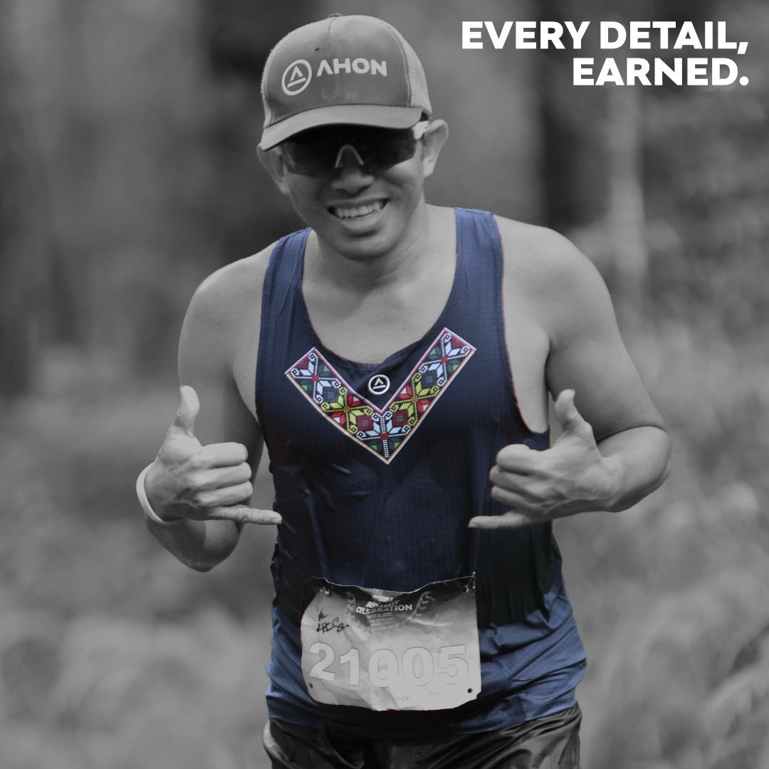 Trail runner wearing Ahon Uleyan Super Light Singlet in dark gray with Filipino-inspired chest pattern, mid-race in forest terrain