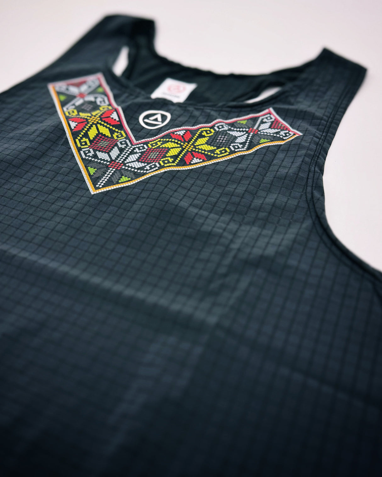 Studio flatlay of ULEYAN Super Light Singlet in dark gray with traditional-inspired front pattern