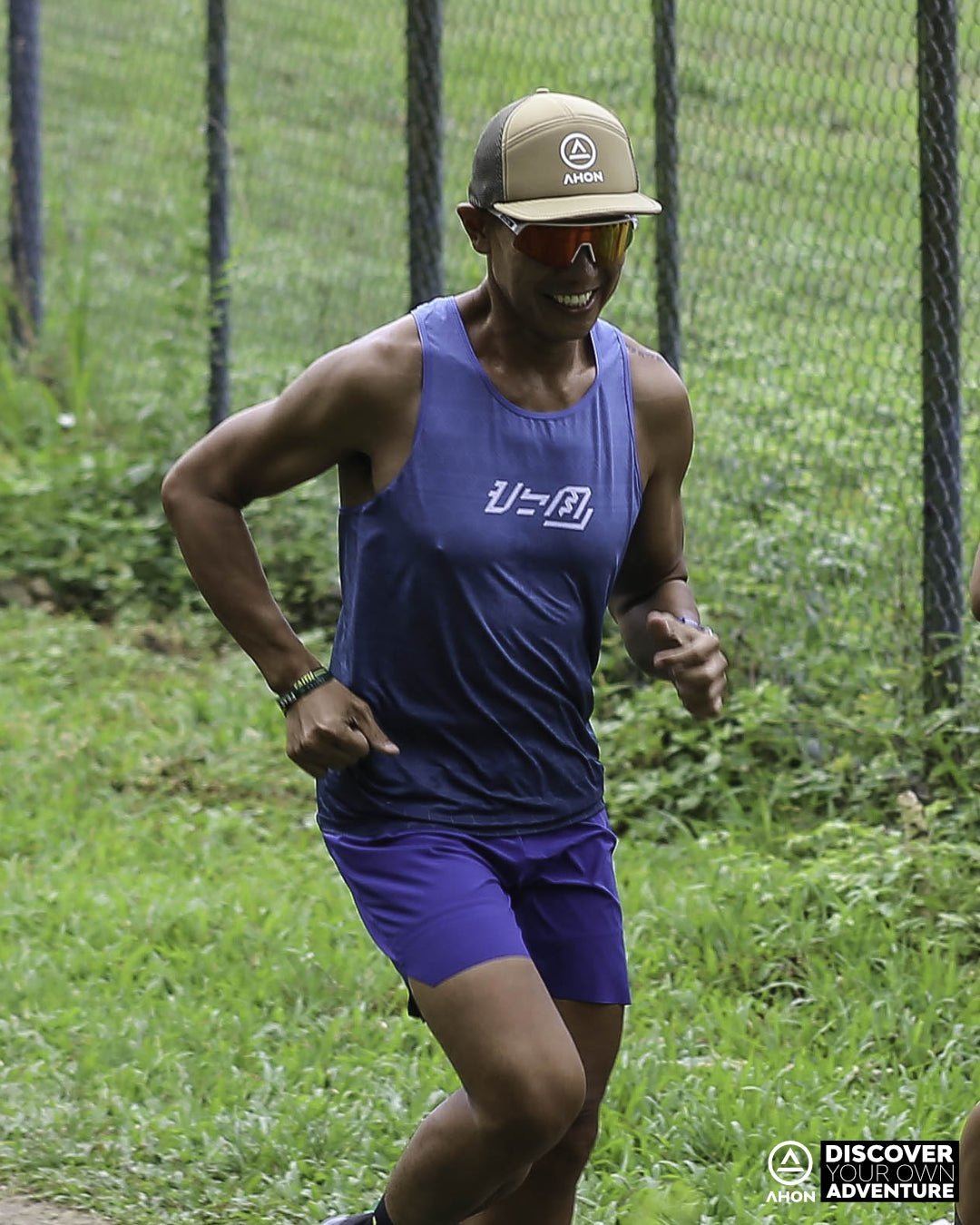 trail runner in Ahon blue green Ultra Light Singlet running through forest trail, wearing a cap and sunglasses