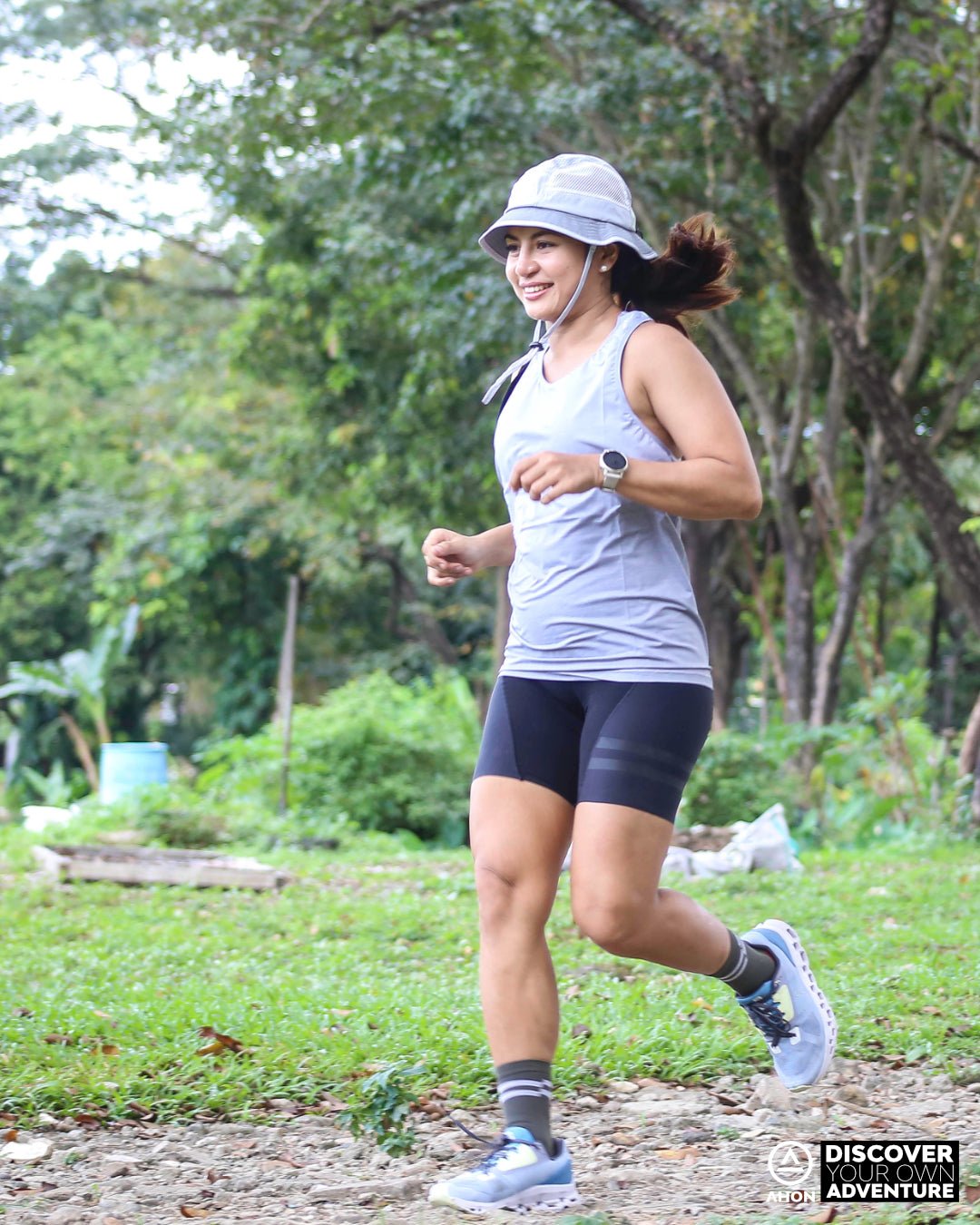 Female trail runner wearing Ahon Ultra Light Singlet in Gray/Yellow with bucket hat on rugged outdoor terrain