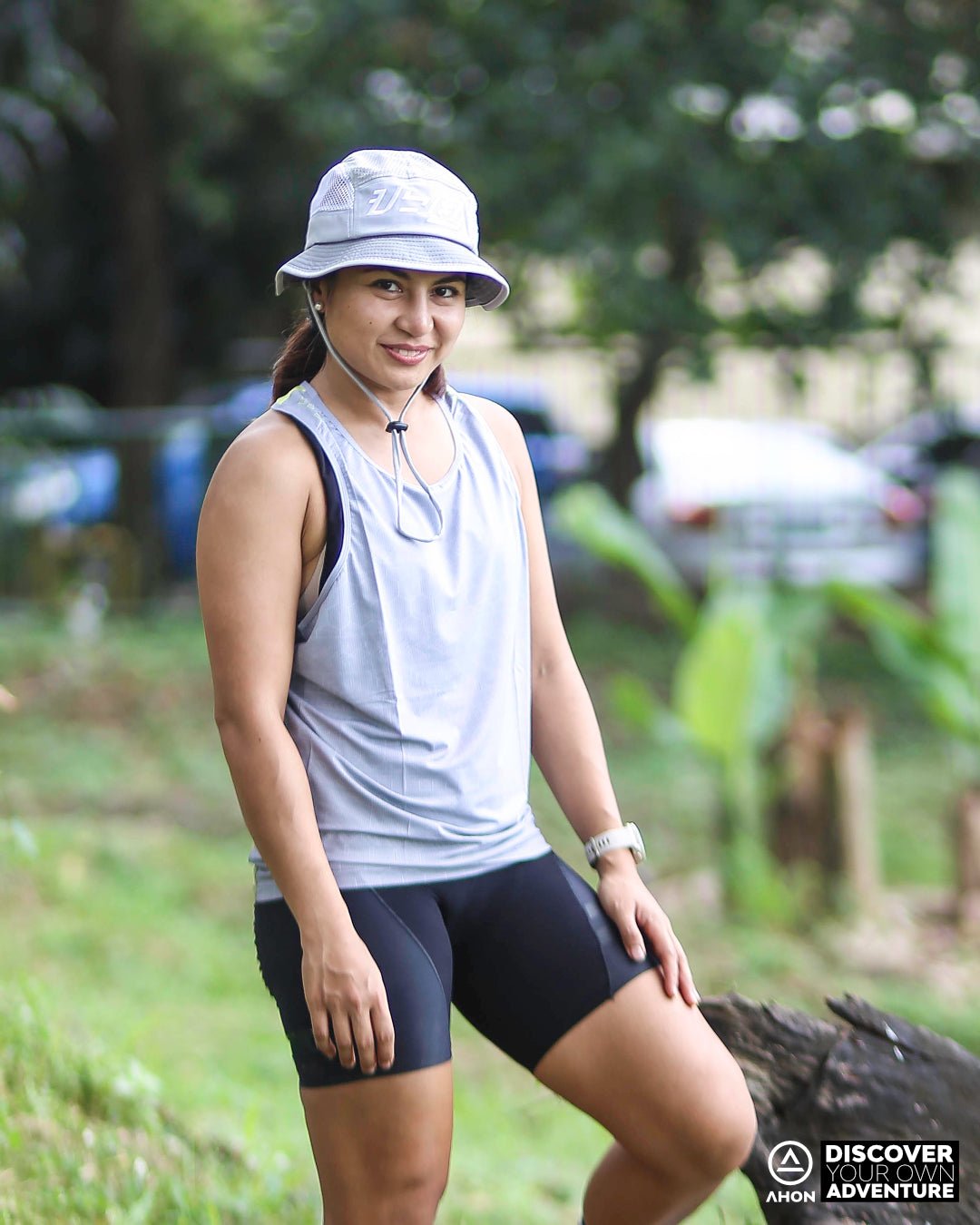 Female trail runner wearing Ahon Ultra Light Singlet in Gray/Yellow with bucket hat on rugged outdoor terrain
