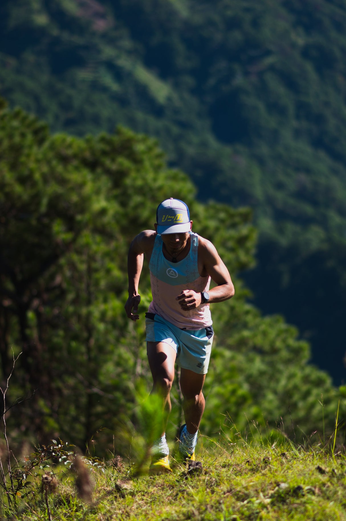 Trail runner climbing a ridge in Singlet Pro Colorway 3 with forest background – front view